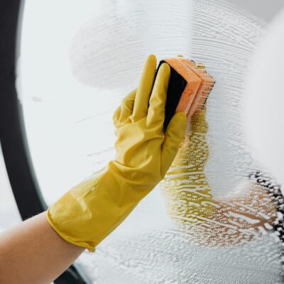 Anonymous person in yellow rubber gloves using simple sponge for cleaning mirror in bathroom