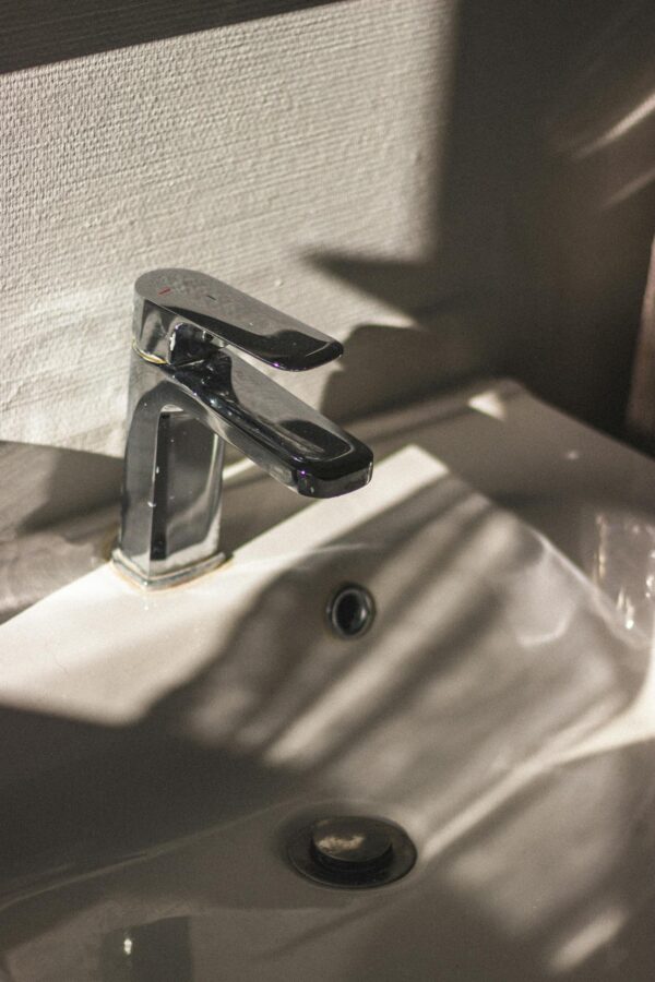 Closeup of chrome single handle faucet installed on white ceramic sink in bathroom at sunlight